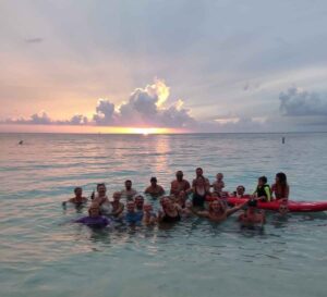 Seven Mile Beach (SMB) is a long crescent of coral-sand beach on the western end of Grand Cayman island. The photo has staff celebrating a birthday on a seven mile stretch of white sandy beach in Cayman Islands